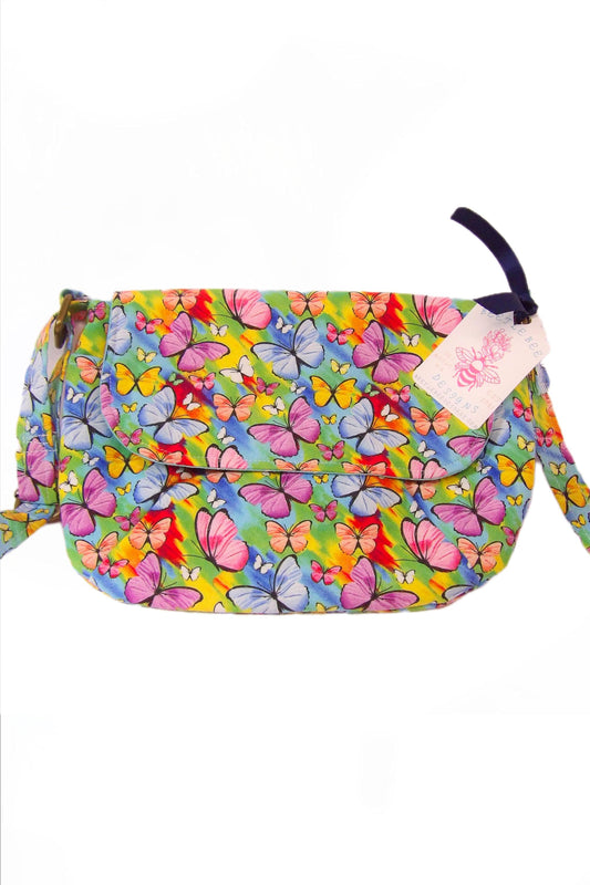 front closed view of crossbody fabric purse with colorful rainbow butterfly design perfect for festivals or day trips. Model wearing lightweight crossbody bag with rainbow butterfly fabric in a bohemian style