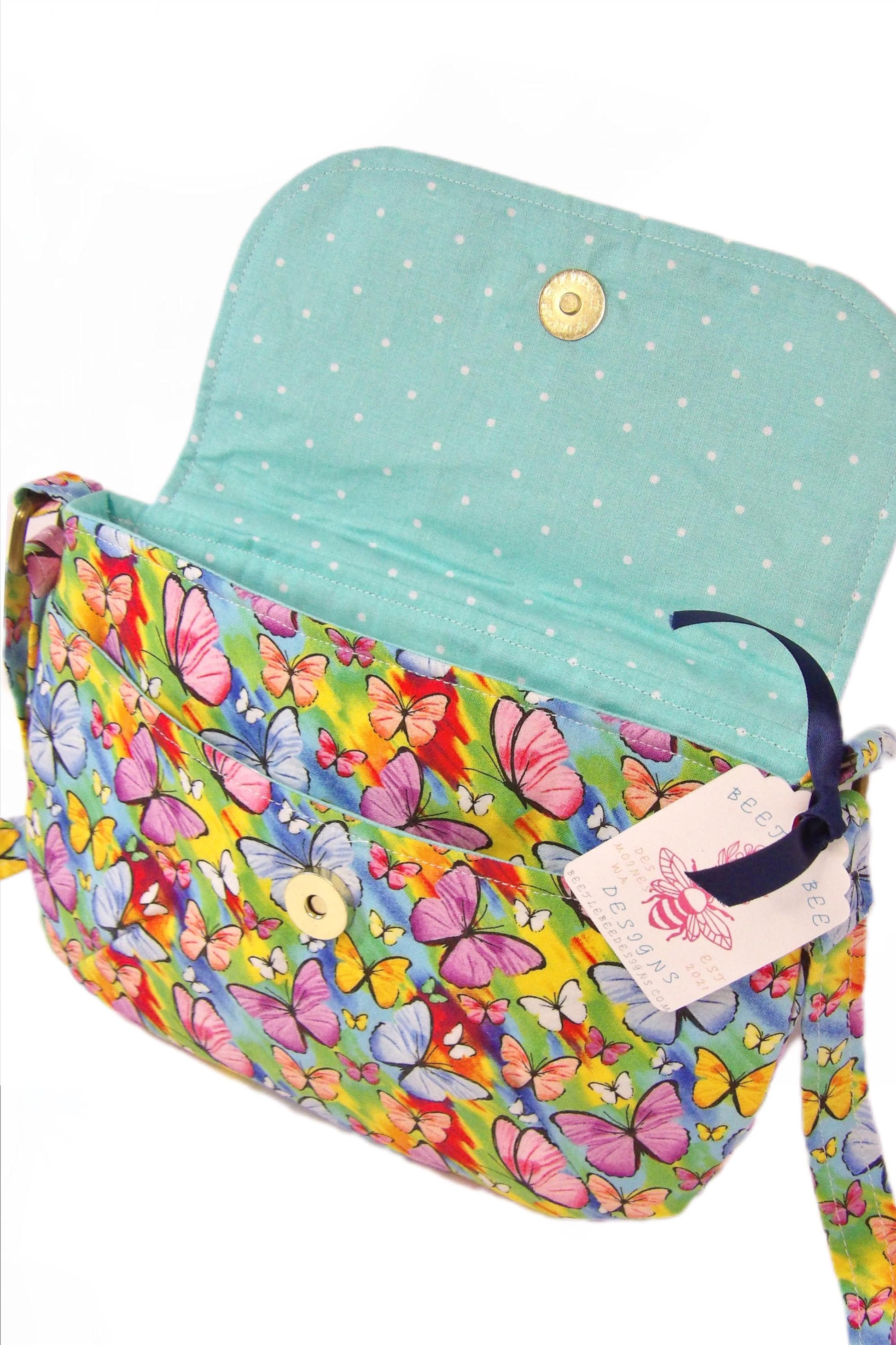 open view from the side of crossbody fabric purse with colorful rainbow butterfly design perfect for festivals or day trips. Model wearing lightweight crossbody bag with rainbow butterfly fabric in a bohemian style