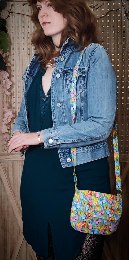 model wearing crossbody fabric purse with colorful rainbow butterfly design perfect for festivals or day trips. Model wearing lightweight crossbody bag with rainbow butterfly fabric in a bohemian style
