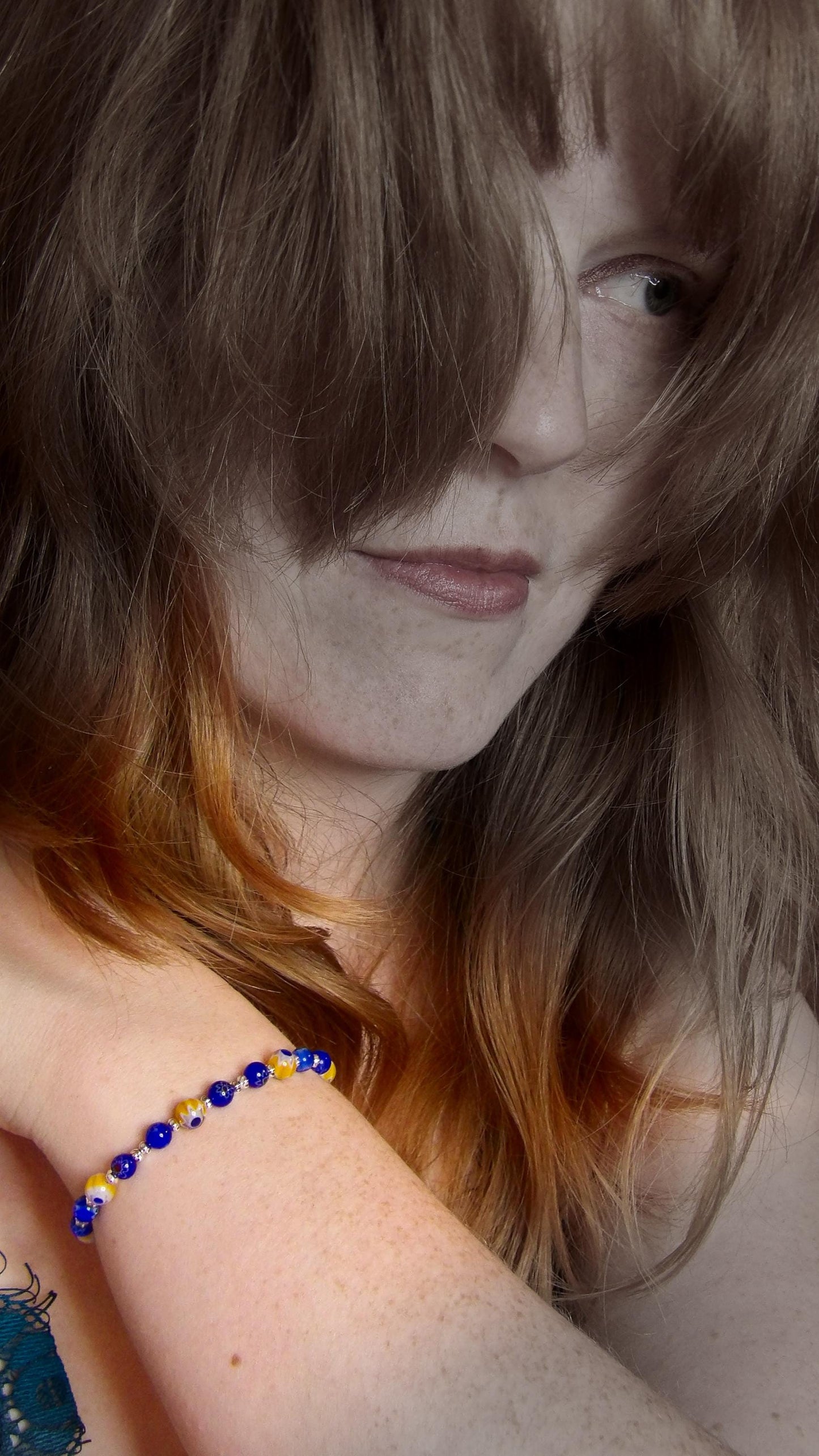 model wearing blue and yellow mosaic glass bracelet made with floral millefiori and star place spacer beads in a bohemian style.