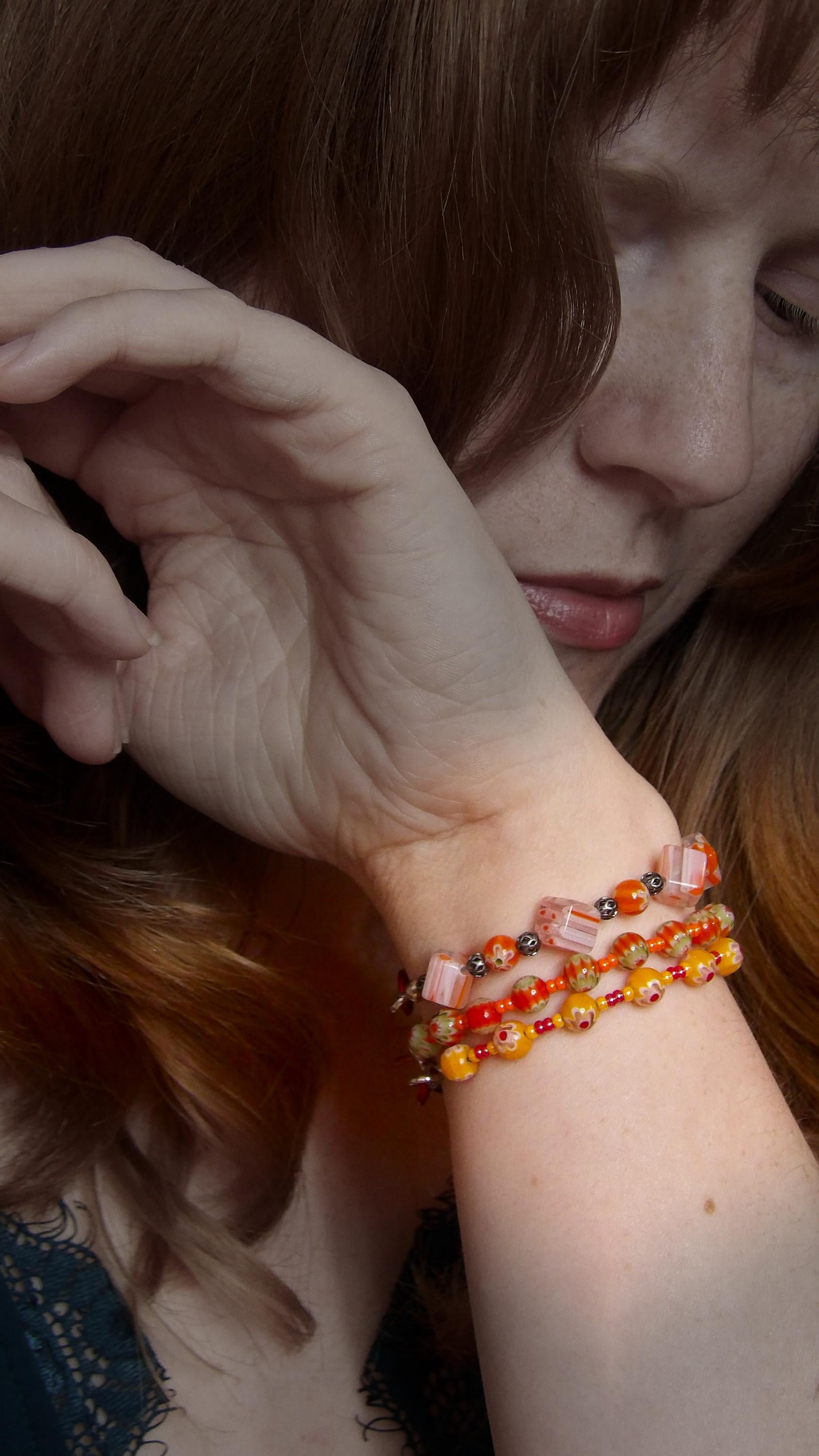 model wearing orange and green millefiori glass beaded bracelet in bohemian style accented by orange czech glass seed beads in a bracelet stack