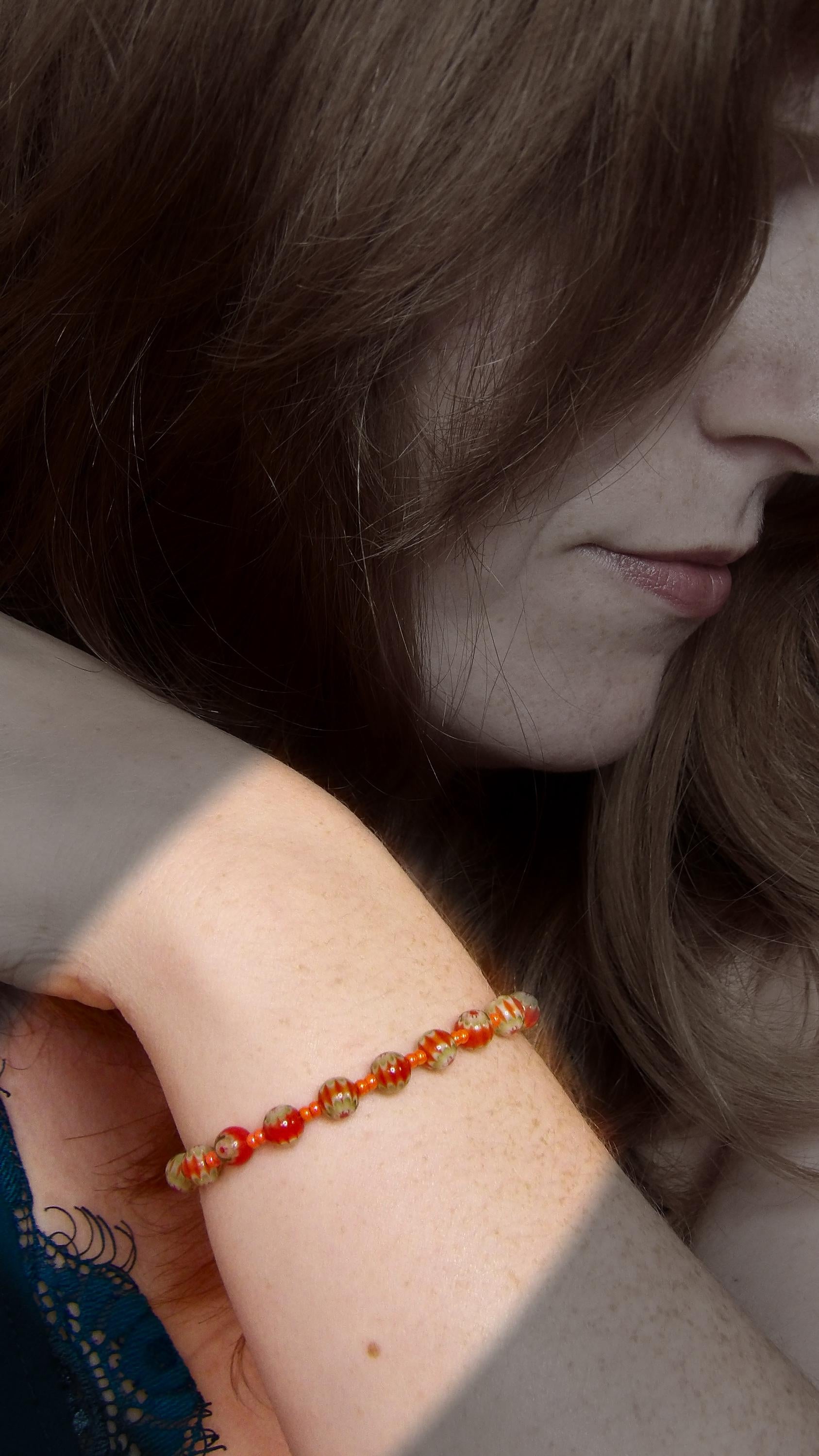 model wearing orange and green millefiori glass beaded bracelet in bohemian style accented by orange czech glass seed beads