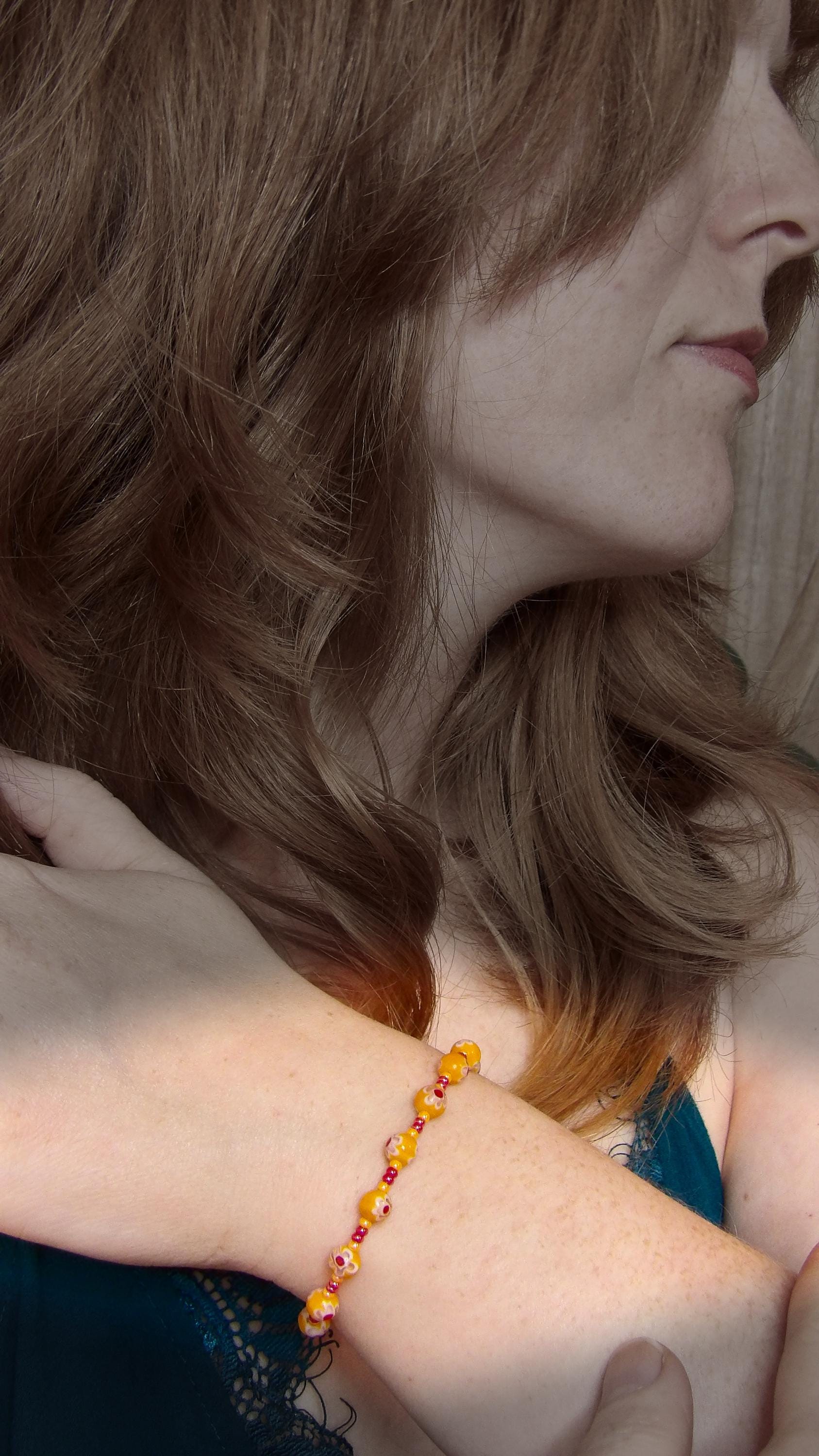 model wearing millefiori glass bracelet made with floral mosaic beads in orange and red. Bohemian style jewelry