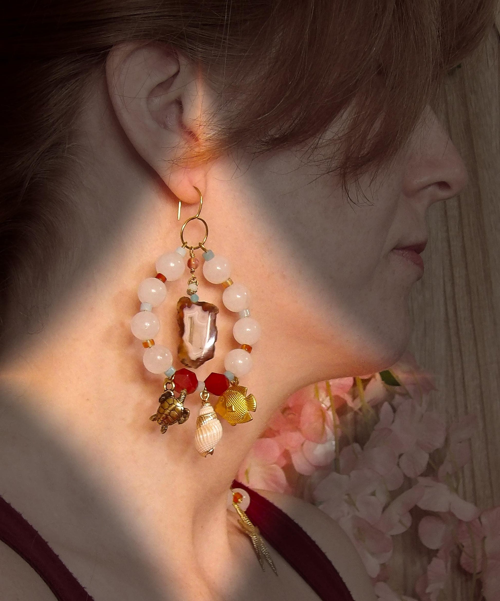 Model wearing asymmetrical earrings with ocean sea life charms, agate slices, white jade, amazonite, carnelian and brass findings. Hand made in USA with ethical gemstones in a boho fashion