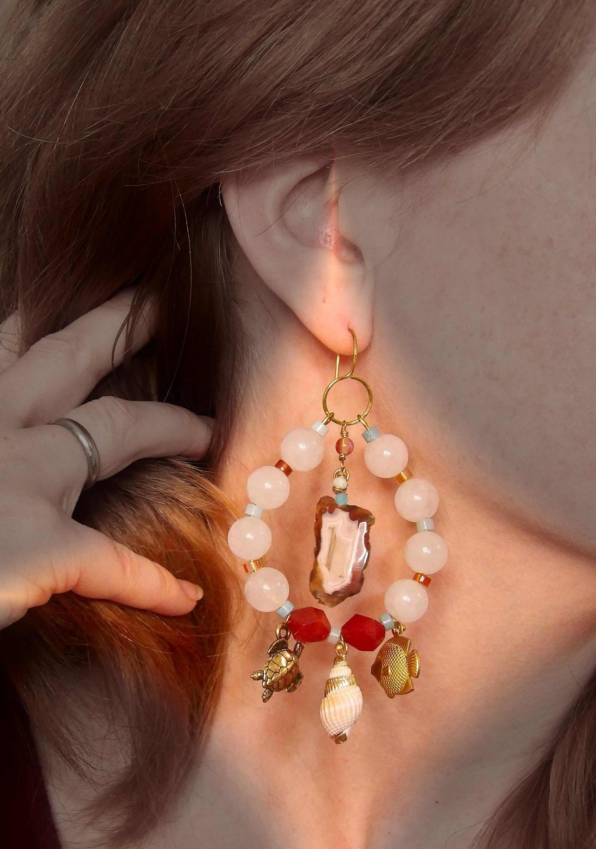 Model wearing asymmetrical earrings with ocean sea life charms, agate slices, white jade, amazonite, carnelian and brass findings. Hand made in USA with ethical gemstones in a boho fashion