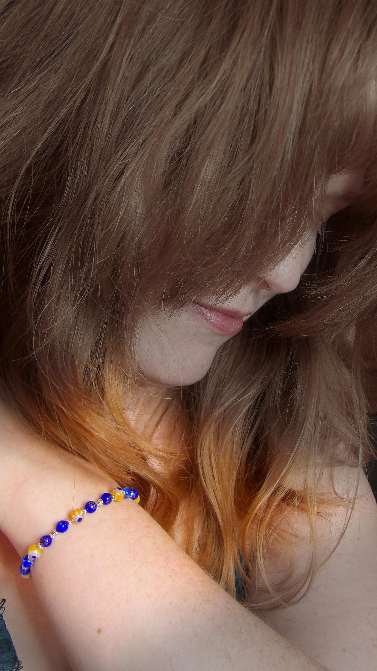 model wearing blue and yellow mosaic glass bracelet made with floral millefiori and star place spacer beads in a bohemian style.