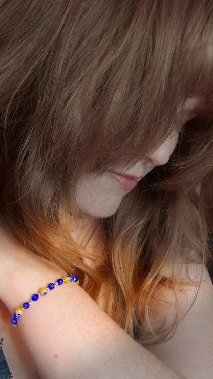 model wearing blue and yellow mosaic glass bracelet made with floral millefiori and star place spacer beads in a bohemian style.