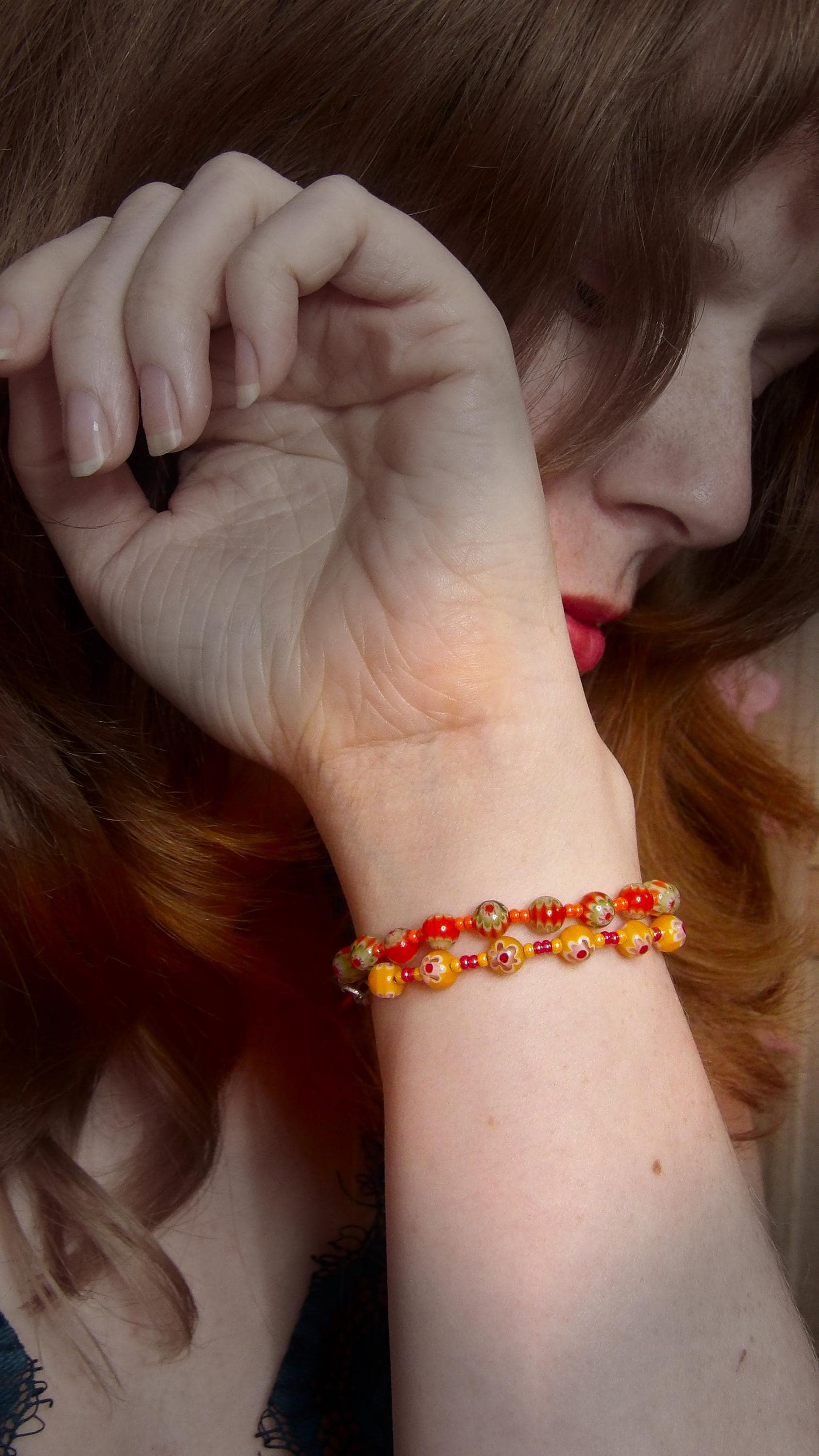 model wearing orange and green millefiori glass beaded bracelet in bohemian style accented by orange czech glass seed beads in a bracelet stack