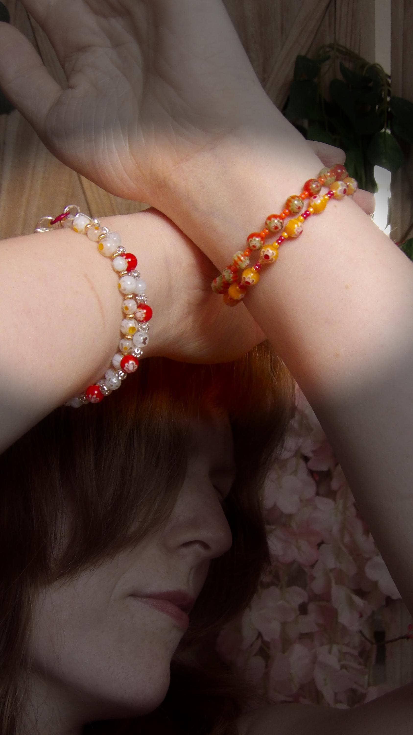 model wearing orange and green millefiori glass beaded bracelet in bohemian style accented by orange czech glass seed beads in a bracelet stack