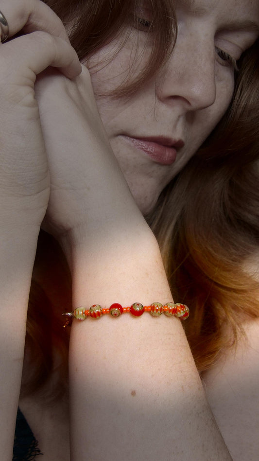 model wearing orange and green millefiori glass beaded bracelet in bohemian style accented by orange czech glass seed beads