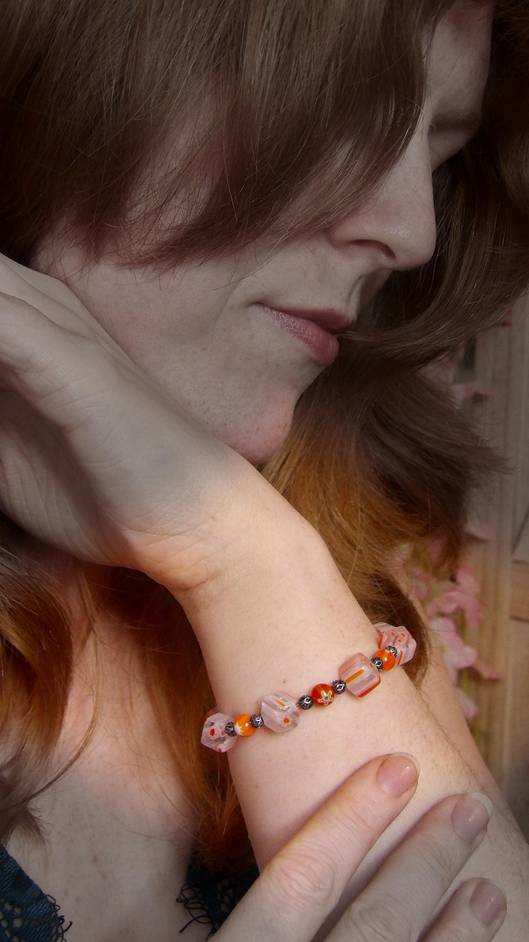 model wearing millefiori glass beaded bracelet made with floral mosaic beads and lace style rounds in a bohemian style. Colors are orange, white and grey.