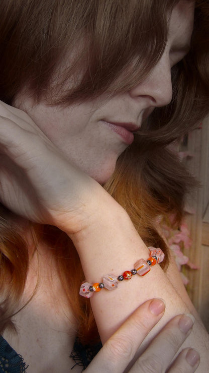 model wearing millefiori glass beaded bracelet made with floral mosaic beads and lace style rounds in a bohemian style. Colors are orange, white and grey.
