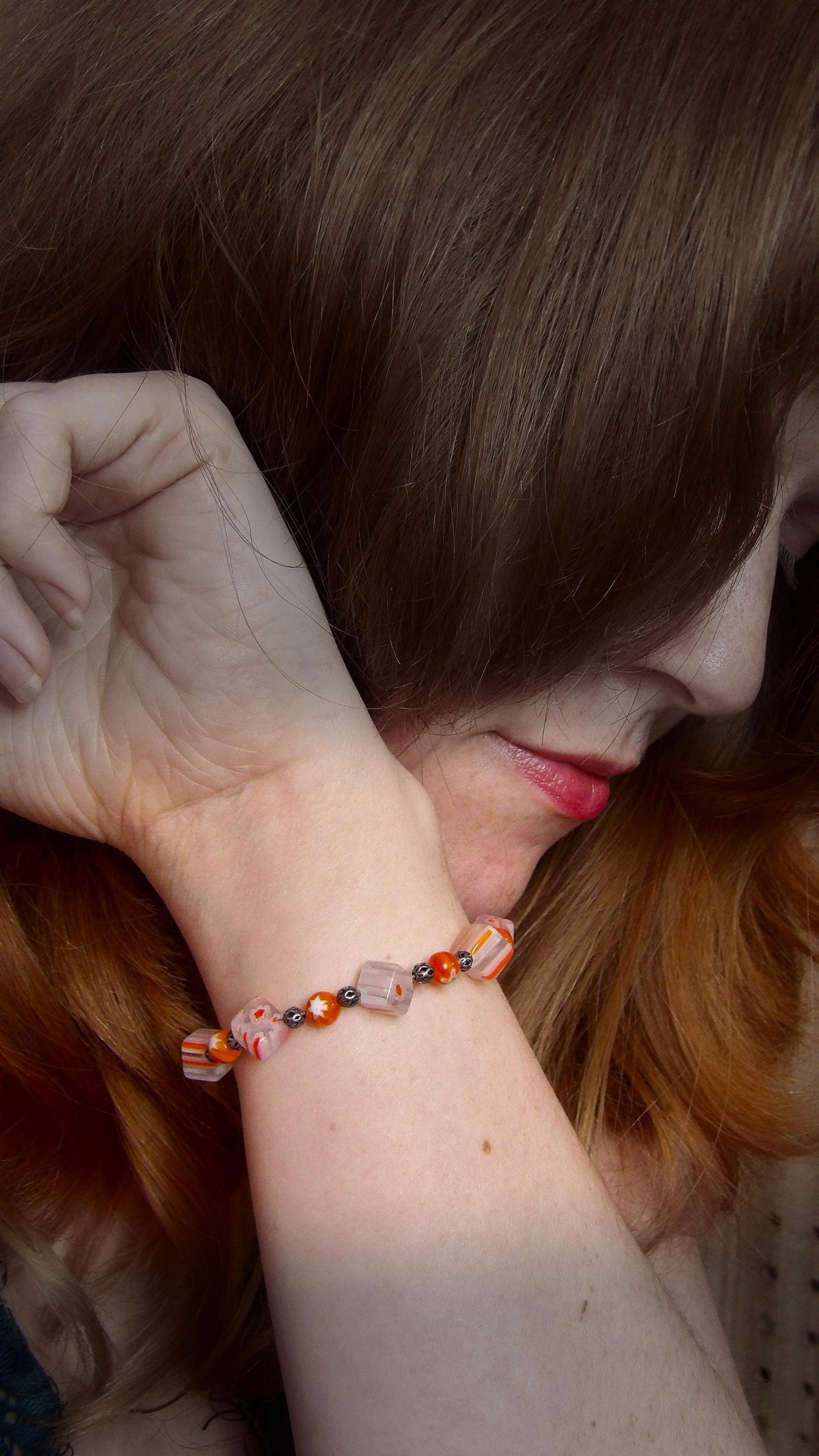 model wearing millefiori glass beaded bracelet made with floral mosaic beads and lace style rounds in a bohemian style. Colors are orange, white and grey.