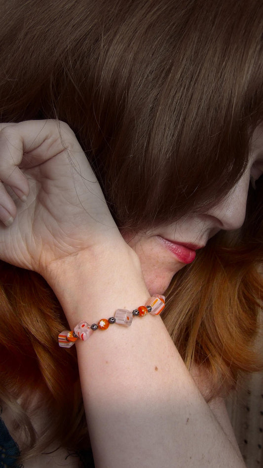 model wearing millefiori glass beaded bracelet made with floral mosaic beads and lace style rounds in a bohemian style. Colors are orange, white and grey.