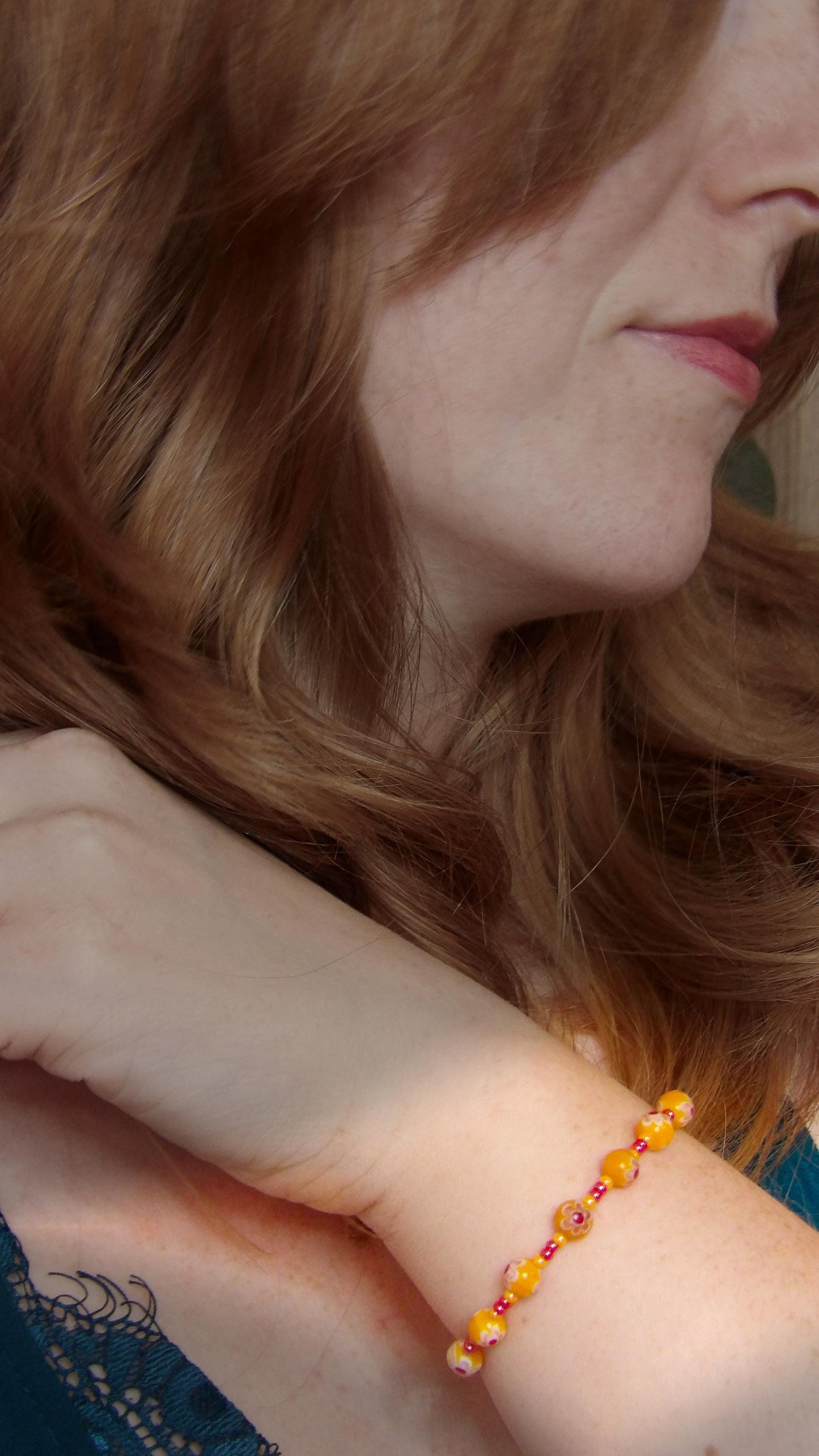 model wearing millefiori glass bracelet made with floral mosaic beads in orange and red. Bohemian style jewelry