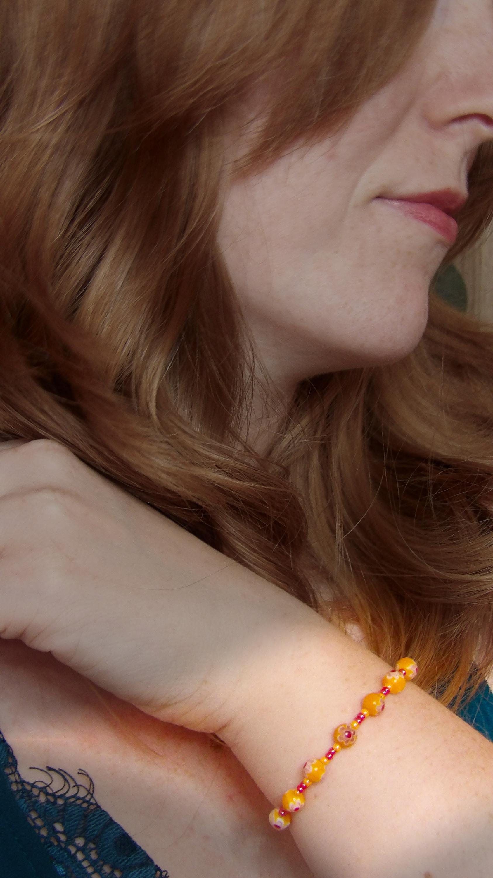 model wearing millefiori glass bracelet made with floral mosaic beads in orange and red. Bohemian style jewelry