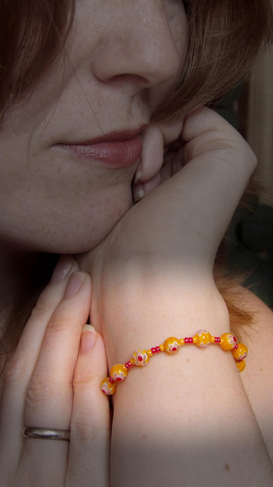 model wearing millefiori glass bracelet made with floral mosaic beads in orange and red. Bohemian style jewelry
