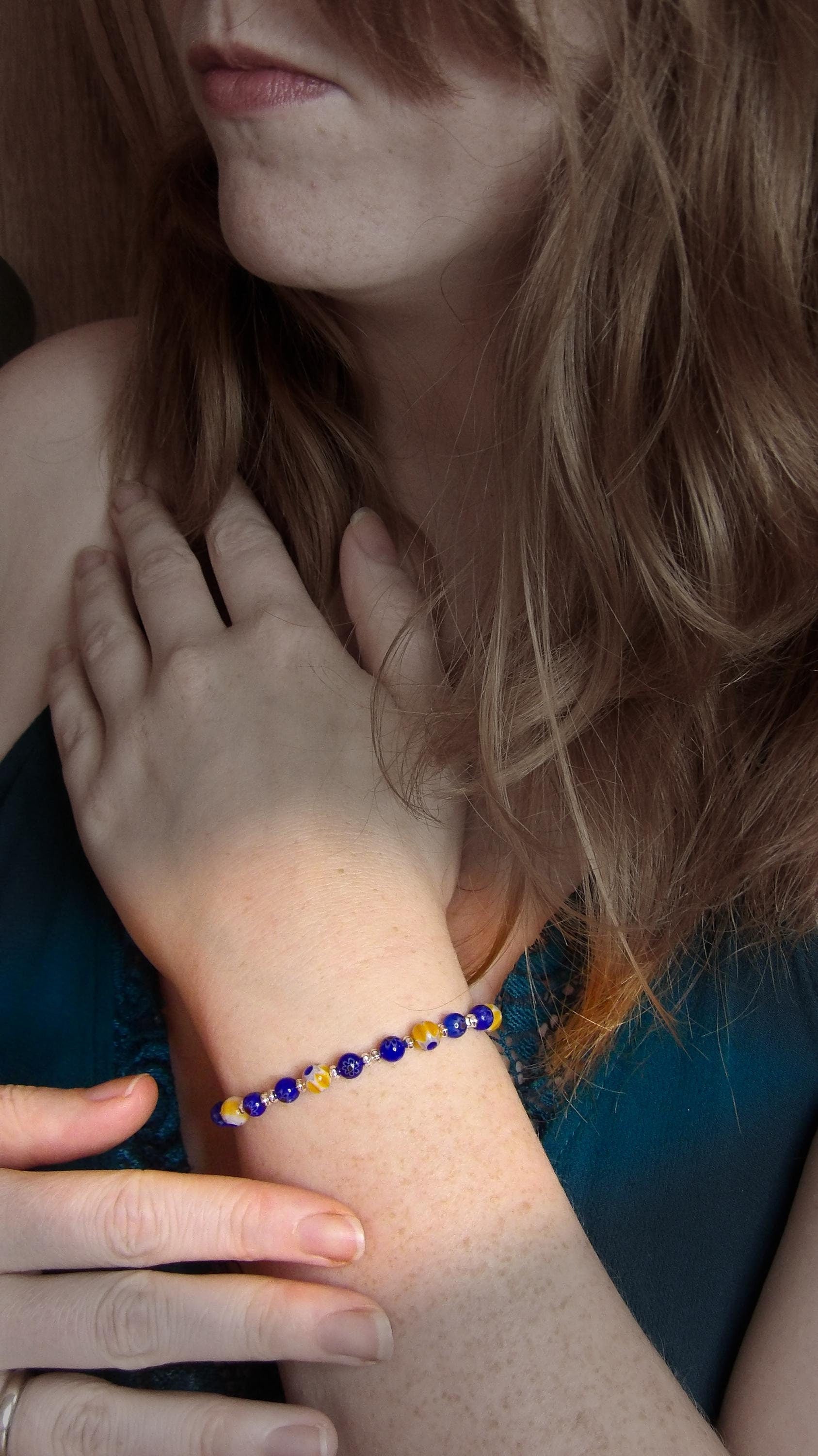 model wearing blue and yellow mosaic glass bracelet made with floral millefiori and star place spacer beads in a bohemian style.