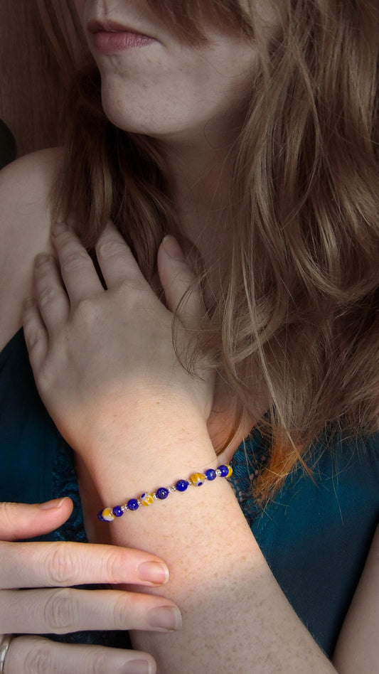 model wearing blue and yellow mosaic glass bracelet made with floral millefiori and star place spacer beads in a bohemian style.