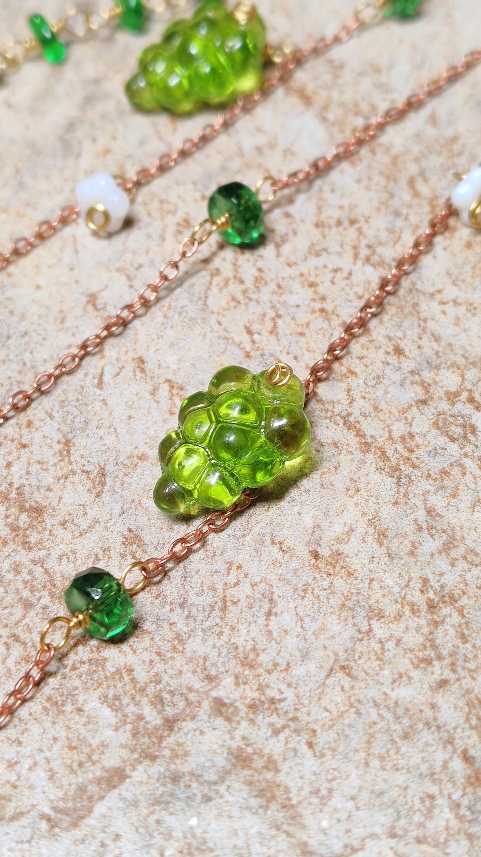 Cottagecore wrap around earring with czech glass flowers and grape beads in shades of green and white. Pierceless design rests behind the ear on a hand forged raw brass frame. Bright copper chains cascade across the top of the ear and from behind the frame for an old world, romantic and rustic vibe. Czech glass beads are hand wrapped and adorned on the the chains throughout the piece