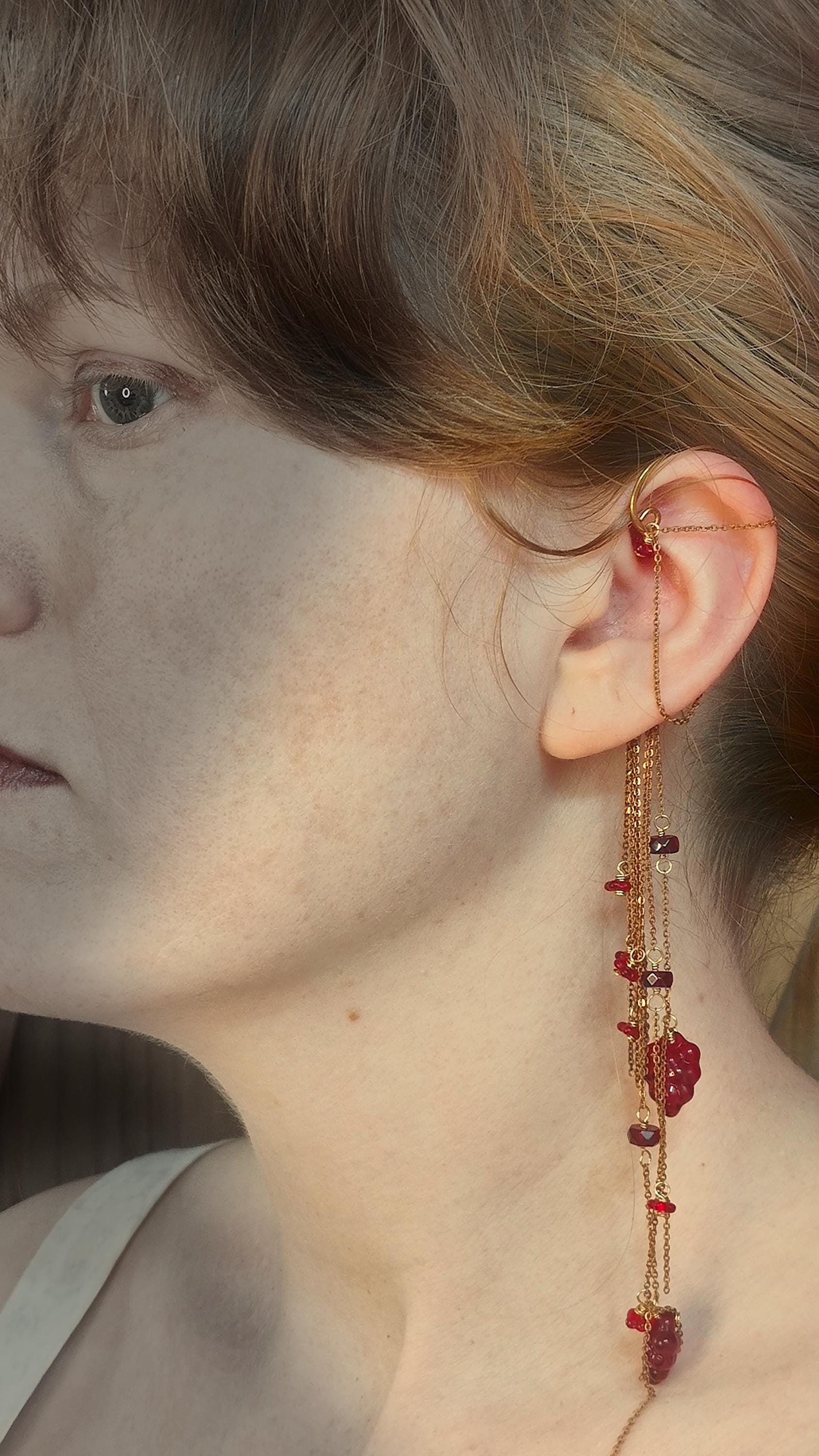 Flower Ear Cuff wrap around earring with red czech glass seed beads. Ear wrap frame sits behind the ear and has chain accents that adorn the top half of the ear along with cascading chains that come from behind the ear. Chains are adorned with hand wrapped czech glass beads in rich red tones. Beads include grape and flower motifs for a rustic, bohemian aura