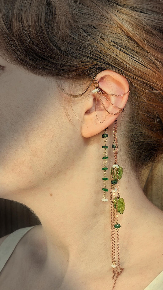 Cottagecore wrap around earring with czech glass flowers and grape beads in shades of green and white. Pierceless design rests behind the ear on a hand forged raw brass frame. Bright copper chains cascade across the top of the ear and from behind the frame for an old world, romantic and rustic vibe. Czech glass beads are hand wrapped and adorned on the the chains throughout the piece